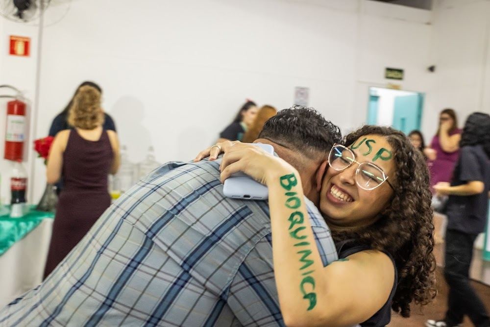 Aluna com Bioquímica escrito no braço comemora com um abraço