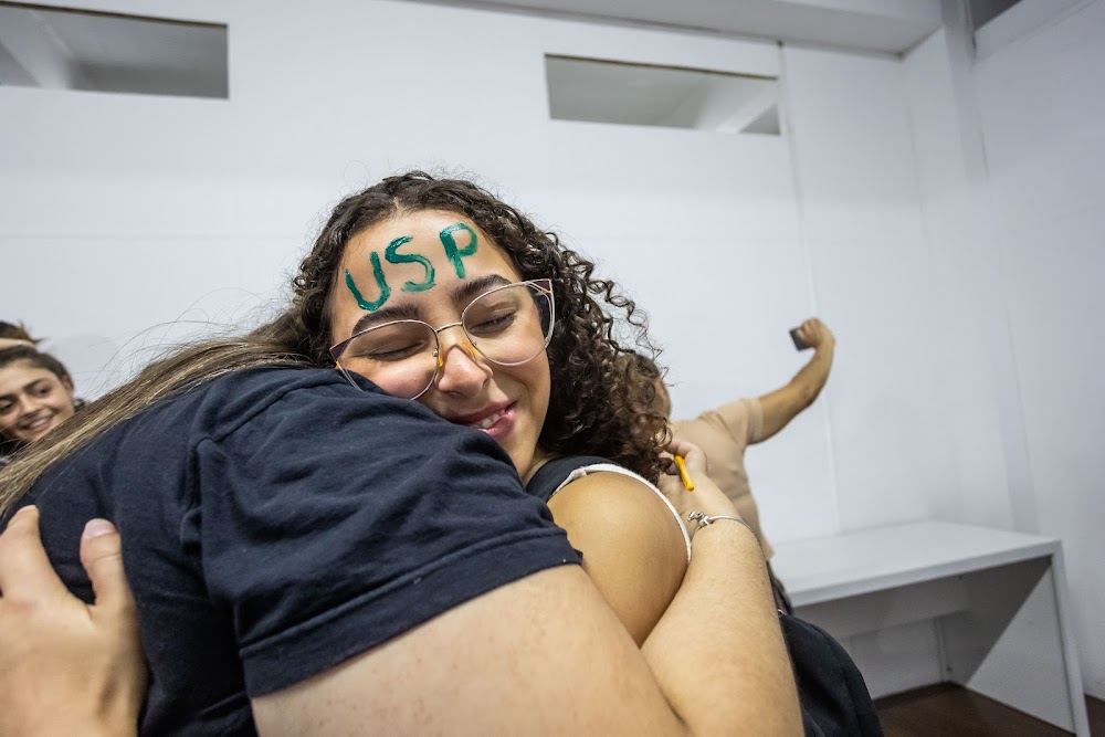 Aluna com USP escrito na testa abraça a família