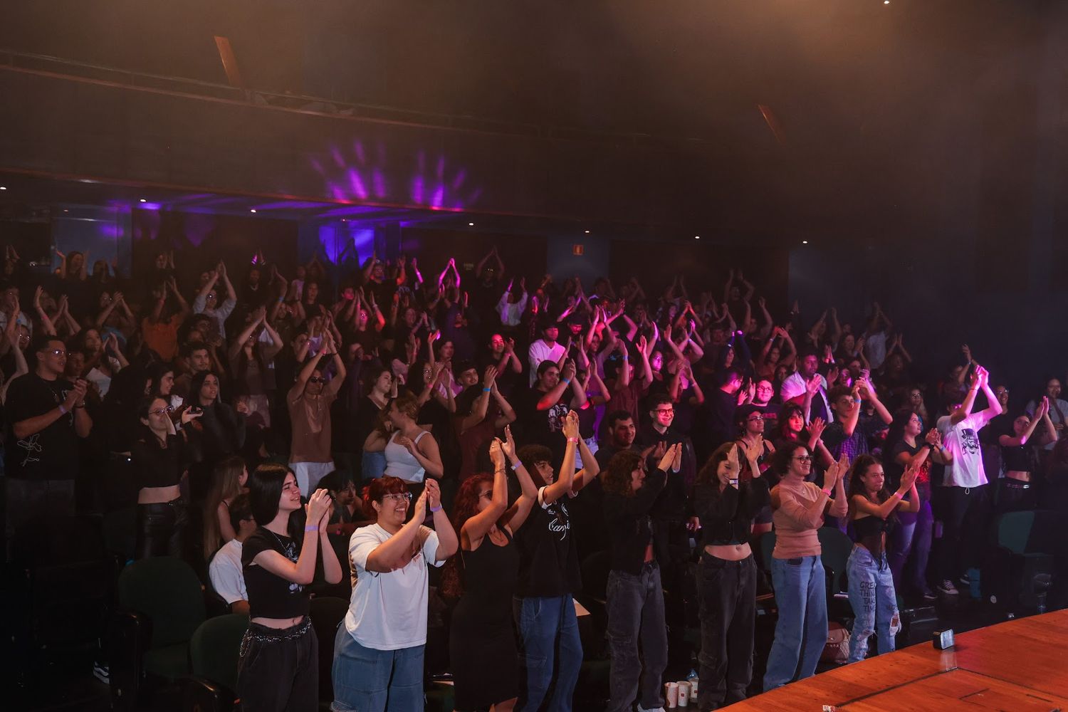 Teatro lotado de estudantes em pé, batendo palmas com as mãos para o alto no Pancadão do ENEM